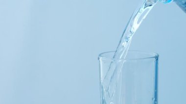 Mavi arka planda şişeden bardağa akan suyun yavaş hareketi.