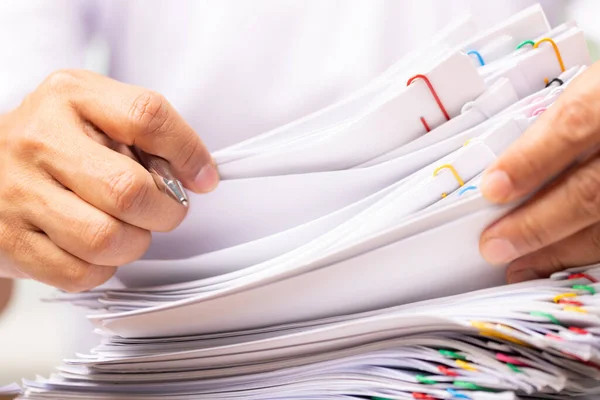 Close-up hands of a man in a white shirt searching for contract agreement documents in Stack of Group report papers clipped in color clipst, business, legal law and education concept.