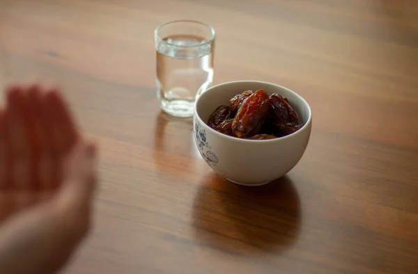 Müslümanlar için Ramazan veya iftar kavramı. İnsan oruç tutmadan önce elleriyle dua eder. Medjool, su, ahşap yemek masasında minimum yemek. Bayram Mübarek.