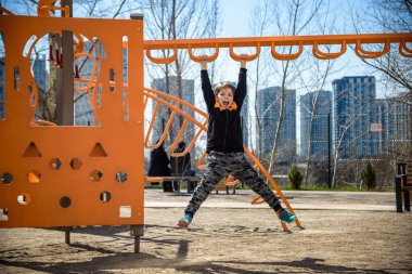 Şirin çocuk okul bahçesinde çocuk parkına tırmanıyor. Çok mutlu bir yüzü var ve bu macera sporlarını tek başına seviyor. Sıcak güneşli bir gün..