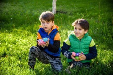 Paskalya yumurtası avındaki çocuklar bahar bahçesinde. Çiçek çayırında renkli yumurta arayan çocuklar. Küçük çocuk ve kardeşi arkadaşı çocuk dışarıda oynuyorlar..