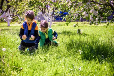 Paskalya yumurtası avındaki çocuklar bahar bahçesinde. Çiçek çayırında renkli yumurta arayan çocuklar. Küçük çocuk ve kardeşi arkadaşı çocuk dışarıda oynuyorlar..