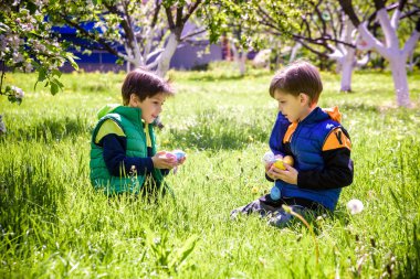 Paskalya yumurtası avındaki çocuklar bahar bahçesinde. Çiçek çayırında renkli yumurta arayan çocuklar. Küçük çocuk ve kardeşi arkadaşı çocuk dışarıda oynuyorlar..