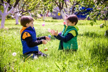Paskalya yumurtası avındaki çocuklar bahar bahçesinde. Çiçek çayırında renkli yumurta arayan çocuklar. Küçük çocuk ve kardeşi arkadaşı çocuk dışarıda oynuyorlar..
