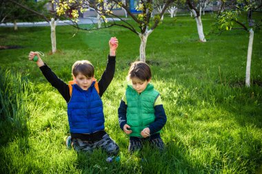 Paskalya yumurtası avındaki çocuklar bahar bahçesinde. Çiçek çayırında renkli yumurta arayan çocuklar. Küçük çocuk ve kardeşi arkadaşı çocuk dışarıda oynuyorlar..