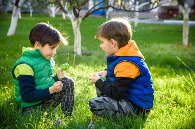 Paskalya yumurtası avındaki çocuklar bahar bahçesinde. Çiçek çayırında renkli yumurta arayan çocuklar. Küçük çocuk ve kardeşi arkadaşı çocuk dışarıda oynuyorlar..