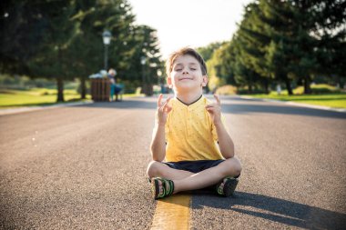 Bir çocuk yolun ortasında asfalt üzerinde oturmuş meditasyon yapıyor. Ruh eğitimi rahatlama kavramı.
