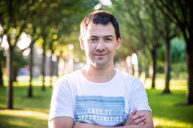 Açık havada beyaz gömlekli, doğa parkında gülümseyen güzel bir adamın portresini kapat. Moda modeli.