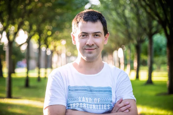 Açık havada beyaz gömlekli, doğa parkında gülümseyen güzel bir adamın portresini kapat. Moda modeli.