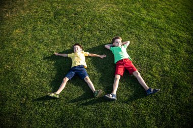 Parkta eğlenen iki kardeşin fotoğrafı, yeşil çimenlere uzanan iki neşeli çocuk, dışarıda oynayan küçük çocuk, en iyi arkadaşlar, mutlu aile, aşk ve mutluluk konsepti..
