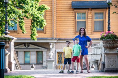 Genç bir kadın çocuklarıyla parkta oynarken eğleniyor. İlkokul çağındaki çocuklar. Aile pitoresk bitkilerle çevrili. Açık hava oyunları herkes için kullanışlı.