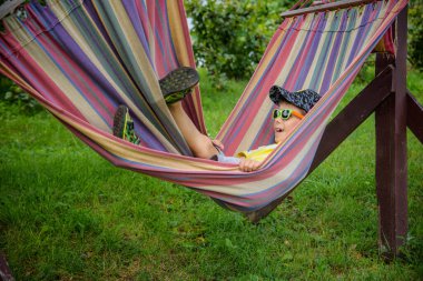 Sevimli beyaz çocuk bahçedeki ya da bahçedeki renkli hamakta rahatlıyor ve eğleniyor. Çocuklar için yaz tatili. Hamakta sallanan çocuk. Çocuklar için etkinlikler.