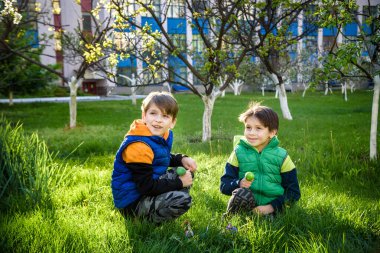 Paskalya yumurtası avındaki çocuklar bahar bahçesinde. Çiçek çayırında renkli yumurta arayan çocuklar. Küçük çocuk ve kardeşi arkadaşı çocuk dışarıda oynuyorlar..