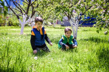 Paskalya yumurtası avındaki çocuklar bahar bahçesinde. Çiçek çayırında renkli yumurta arayan çocuklar. Küçük çocuk ve kardeşi arkadaşı çocuk dışarıda oynuyorlar..