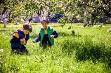 Paskalya yumurtası avındaki çocuklar bahar bahçesinde. Çiçek çayırında renkli yumurta arayan çocuklar. Küçük çocuk ve kardeşi arkadaşı çocuk dışarıda oynuyorlar..