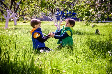 Paskalya yumurtası avındaki çocuklar bahar bahçesinde. Çiçek çayırında renkli yumurta arayan çocuklar. Küçük çocuk ve kardeşi arkadaşı çocuk dışarıda oynuyorlar..
