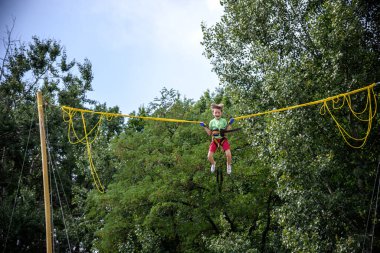 Çocuk bungee trambolinde zıplıyor. Sigortası ve esneyebilir lastikleri olan bir çocuk gökyüzüne asılı duruyor. Eğlence parkında mutlu çocukluk ve oyun kavramı.