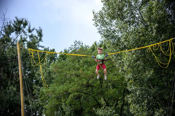 Çocuk bungee trambolinde zıplıyor. Sigortası ve esneyebilir lastikleri olan bir çocuk gökyüzüne asılı duruyor. Eğlence parkında mutlu çocukluk ve oyun kavramı.