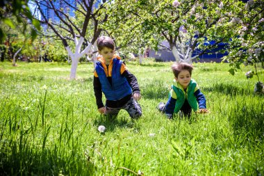 Paskalya yumurtası avındaki çocuklar bahar bahçesinde. Çiçek çayırında renkli yumurta arayan çocuklar. Küçük çocuk ve kardeşi arkadaşı çocuk dışarıda oynuyorlar..