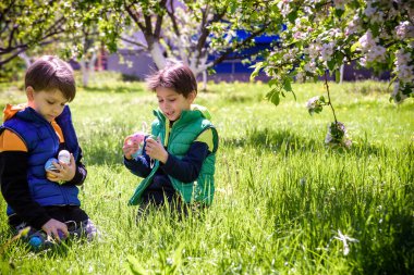 Paskalya yumurtası avındaki çocuklar bahar bahçesinde. Çiçek çayırında renkli yumurta arayan çocuklar. Küçük çocuk ve kardeşi arkadaşı çocuk dışarıda oynuyorlar..