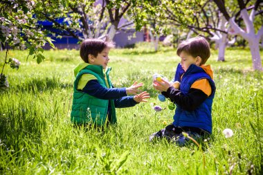 Paskalya yumurtası avındaki çocuklar bahar bahçesinde. Çiçek çayırında renkli yumurta arayan çocuklar. Küçük çocuk ve kardeşi arkadaşı çocuk dışarıda oynuyorlar..
