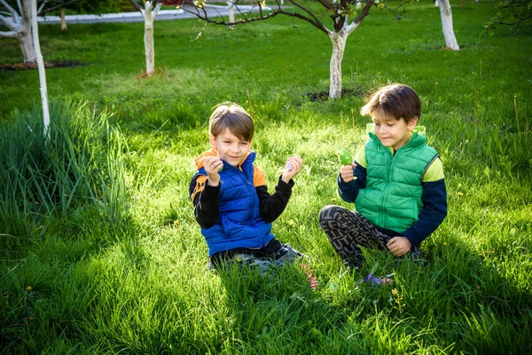 Paskalya yumurtası avındaki çocuklar bahar bahçesinde. Çiçek çayırında renkli yumurta arayan çocuklar. Küçük çocuk ve kardeşi arkadaşı çocuk dışarıda oynuyorlar..