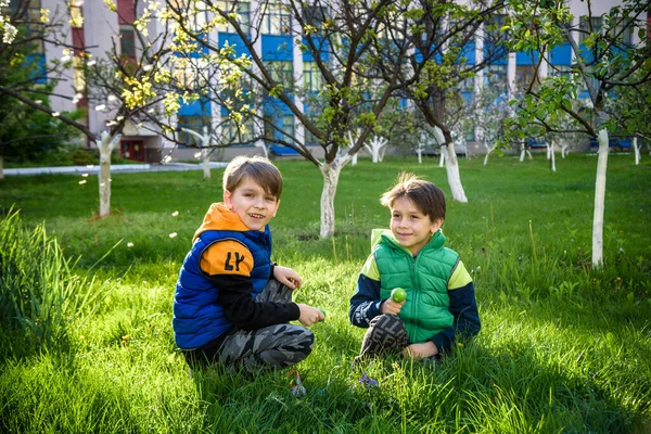 Paskalya yumurtası avındaki çocuklar bahar bahçesinde. Çiçek çayırında renkli yumurta arayan çocuklar. Küçük çocuk ve kardeşi arkadaşı çocuk dışarıda oynuyorlar..
