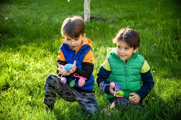 Paskalya yumurtası avındaki çocuklar bahar bahçesinde. Çiçek çayırında renkli yumurta arayan çocuklar. Küçük çocuk ve kardeşi arkadaşı çocuk dışarıda oynuyorlar..