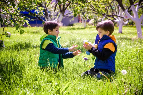 Paskalya yumurtası avındaki çocuklar bahar bahçesinde. Çiçek çayırında renkli yumurta arayan çocuklar. Küçük çocuk ve kardeşi arkadaşı çocuk dışarıda oynuyorlar..