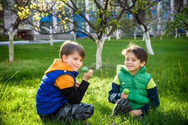 Paskalya yumurtası avındaki çocuklar bahar bahçesinde. Çiçek çayırında renkli yumurta arayan çocuklar. Küçük çocuk ve kardeşi arkadaşı çocuk dışarıda oynuyorlar..