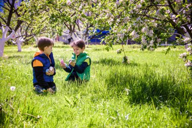 Paskalya yumurtası avındaki çocuklar bahar bahçesinde. Çiçek çayırında renkli yumurta arayan çocuklar. Küçük çocuk ve kardeşi arkadaşı çocuk dışarıda oynuyorlar..