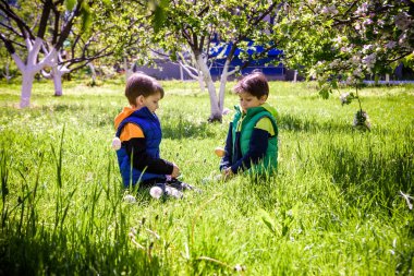 Paskalya yumurtası avındaki çocuklar bahar bahçesinde. Çiçek çayırında renkli yumurta arayan çocuklar. Küçük çocuk ve kardeşi arkadaşı çocuk dışarıda oynuyorlar..