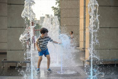 Boy having fun in water fountains. Child playing with a city fountain on hot summer day. Happy kids having fun in fountain. Summer weather. Active leisure, lifestyle and vacation.