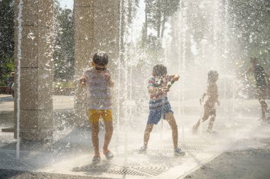 Boy having fun in water fountains. Child playing with a city fountain on hot summer day. Happy kids having fun in fountain. Summer weather. Active leisure, lifestyle and vacation.