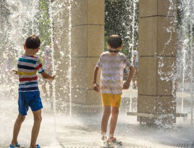 Boy having fun in water fountains. Child playing with a city fountain on hot summer day. Happy kids having fun in fountain. Summer weather. Active leisure, lifestyle and vacation.