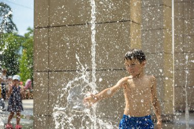 Boy having fun in water fountains. Child playing with a city fountain on hot summer day. Happy kids having fun in fountain. Summer weather. Active leisure, lifestyle and vacation.