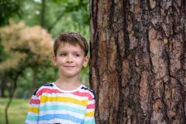 Küçük çocuk bir ağaç gövdesine sarılıyor - çocuklar doğayı seviyor, sürdürülebilirlik kavramını. Gülümseyen mutlu çocuk doğrudan kameraya bak. Doğayı kurtar..