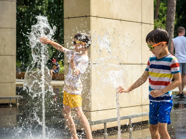 Çocuk çeşmelerde eğleniyor. Sıcak bir yaz gününde şehir çeşmesiyle oynayan bir çocuk. Fıskiyede eğlenen mutlu çocuklar. Yaz havası. Aktif eğlence, yaşam tarzı ve tatil.