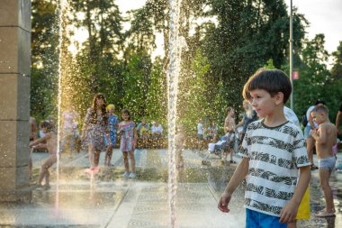 Kyiv, Ukrayna - 01 Ağustos 2021: Çeşmelere atlayan çocuklar. Çocuklar sıcak yaz gününde şehir çeşmesiyle oynuyorlar. Mutlu arkadaşlar çeşmede eğleniyor. Yaz havası. Arkadaşlık, yaşam tarzı ve tatil.