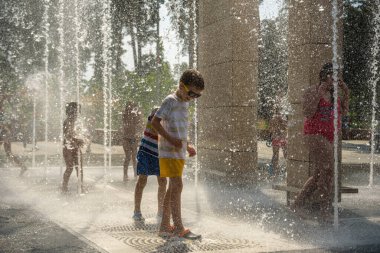 Kyiv, Ukrayna - 01 Ağustos 2021: Çeşmelere atlayan çocuklar. Çocuklar sıcak yaz gününde şehir çeşmesiyle oynuyorlar. Mutlu arkadaşlar çeşmede eğleniyor. Yaz havası. Arkadaşlık, yaşam tarzı ve tatil.