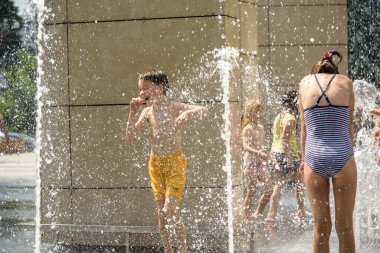 Kyiv, Ukrayna - 01 Ağustos 2021: Çeşmelere atlayan çocuklar. Çocuklar sıcak yaz gününde şehir çeşmesiyle oynuyorlar. Mutlu arkadaşlar çeşmede eğleniyor. Yaz havası. Arkadaşlık, yaşam tarzı ve tatil.