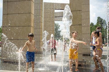 Kyiv, Ukraine - August 01, 2021: Boys jumping in water fountains. Children playing with a city fountain on hot summer day. Happy friends having fun in fountain. Summer weather. Friendship, lifestyle and vacation.