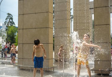 Kyiv, Ukraine - August 01, 2021: Boys jumping in water fountains. Children playing with a city fountain on hot summer day. Happy friends having fun in fountain. Summer weather. Friendship, lifestyle and vacation.