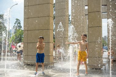 Kyiv, Ukraine - August 01, 2021: Boys jumping in water fountains. Children playing with a city fountain on hot summer day. Happy friends having fun in fountain. Summer weather. Friendship, lifestyle and vacation.