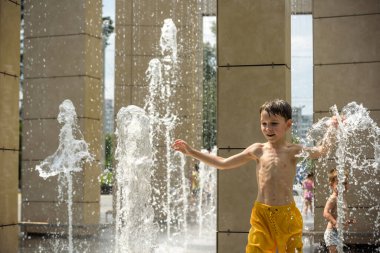 Kyiv, Ukraine - August 01, 2021: Boys jumping in water fountains. Children playing with a city fountain on hot summer day. Happy friends having fun in fountain. Summer weather. Friendship, lifestyle and vacation.