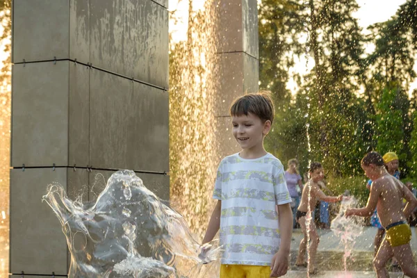 Kyiv, Ukrayna - 01 Ağustos 2021: Çeşmelere atlayan çocuklar. Çocuklar sıcak yaz gününde şehir çeşmesiyle oynuyorlar. Mutlu arkadaşlar çeşmede eğleniyor. Yaz havası. Arkadaşlık, yaşam tarzı ve tatil.