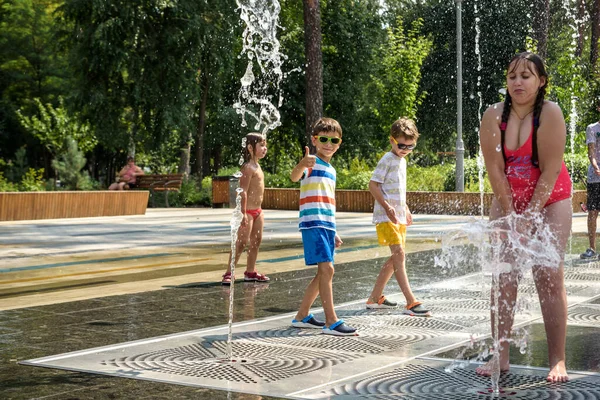 Kyiv, Ukrayna - 01 Ağustos 2021: Çeşmelere atlayan çocuklar. Çocuklar sıcak yaz gününde şehir çeşmesiyle oynuyorlar. Mutlu arkadaşlar çeşmede eğleniyor. Yaz havası. Arkadaşlık, yaşam tarzı ve tatil.