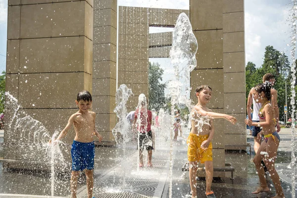 Kyiv, Ukrayna - 01 Ağustos 2021: Çeşmelere atlayan çocuklar. Çocuklar sıcak yaz gününde şehir çeşmesiyle oynuyorlar. Mutlu arkadaşlar çeşmede eğleniyor. Yaz havası. Arkadaşlık, yaşam tarzı ve tatil.