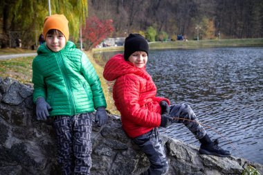 İki kardeş köprüde duruyor ve sonbahar ormanının muhteşem manzarasına ve göldeki sudaki yansımasına hayran kalıyorlar. Sonbahar yürüyüşü. Açık hava yaşam tarzı, aktif aile yaşam tarzı..