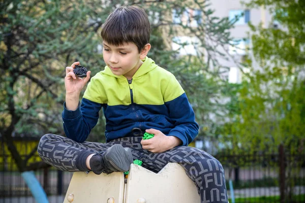 Boy playing with modern spin top outdoors. Entertainment game for children. Top, triggered by a trigger. Kid demonstrate two different variants choosing which is better.